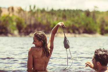 Frau im See, die ihr Bikinioberteil hält und mit ihrem Freund lächelt. Verliebtes Paar, das seinen Sommerurlaub an einem See genießt. - JLPSF18189