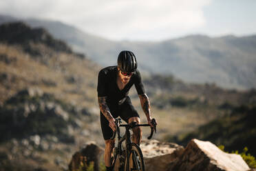 Männlicher Radfahrer fährt hart auf einem Profirad auf einer Bergstraße. Aktiver Sportler, der mit dem Rennrad im Freien fährt. - JLPSF18194