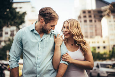 Smiling woman walking on street with her partner holding his hand. Couple in cheerful mood walking on street looking at each other. - JLPSF18197