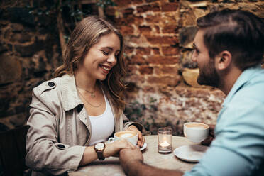 Man holding the hand of his girlfriend sitting at a restaurant. Couple in love sitting at a coffee shop holding hands while drinking coffee. - JLPSF18203