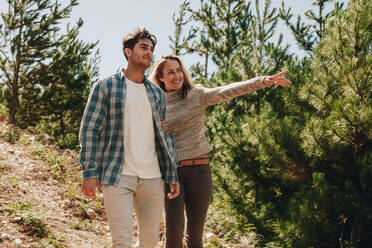 Junger Mann und Frau gehen in den Bergen spazieren, wobei die Frau auf eine Aussicht zeigt. Ein Paar betrachtet eine schöne Aussicht beim Wandern in der Natur. - JLPSF18215