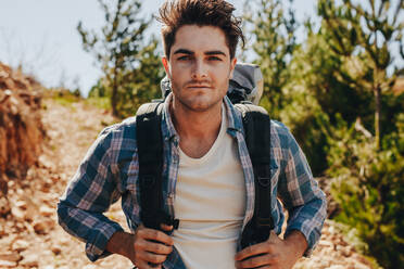 Handsome young guy with backpack walking down the mountain trail. Male hiking in nature on a summer day. - JLPSF18225