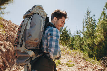 Rear view shot of smiling young guy with backpack hiking on mountains. Caucasian male hiker trekking on mountain. - JLPSF18226