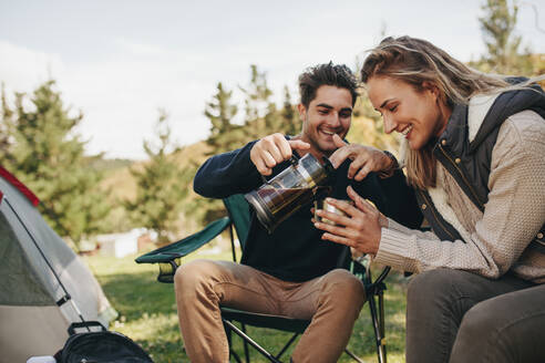 Schönes junges Paar trinkt Kaffee beim Camping in der Natur. Mann gießt Kaffee in die Tasse der Frau. - JLPSF18229