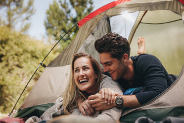 Lächelndes junges Paar, das in einem Zelt liegt. Glückliches Liebespaar, das sich in einem Zelt auf einem Campingplatz ausruht. - JLPSF18236