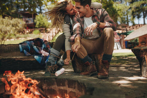 Romantisches Paar sitzt am Lagerfeuer und röstet Marshmallows auf dem Feuer. Schönes verliebtes Paar genießt auf dem Campingplatz. - JLPSF18241