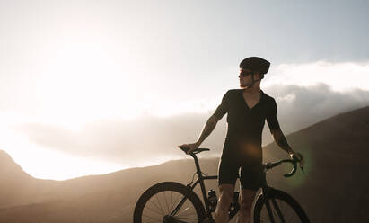Profi-Radfahrer, der eine Pause macht, während er in der Natur fährt. Männlicher Radfahrer, der mit seinem Fahrrad auf der Landstraße an einem sonnigen Tag steht. - JLPSF18330