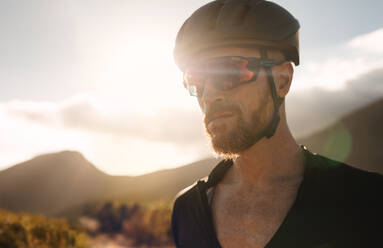 Nahaufnahme eines männlichen Sportlers mit Fahrradhelm und Sonnenbrille. Männlicher Radfahrer an einem sonnigen Tag im Freien. - JLPSF18331