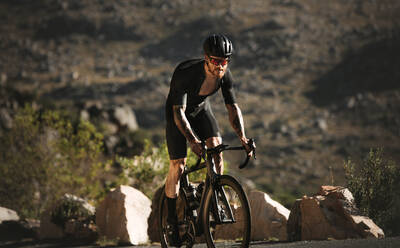 Männlicher Radfahrer, der eine Bergstraße hinauffährt. Entschlossener Sportler, der beim Training bergauf fährt. - JLPSF18343