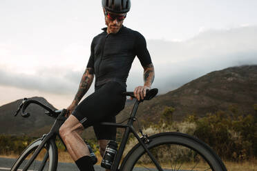 Radsportler in kompletter Profimontur beim Training im Freien. Sportler steht mit seinem Profirad auf einer Bergstraße. - JLPSF18378