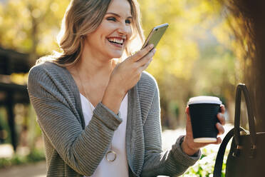 Woman sitting outdoors talking on phone. Female with coffee having a phone call outside in the city. - JLPSF18396