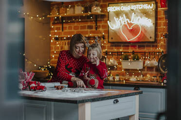 Mutter und Tochter kochen zusammen auf einer Kücheninsel in der Weihnachtszeit - MDOF00154