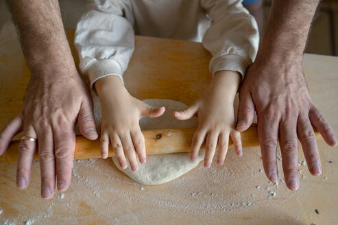 Hände von Sohn und Vater rollen Pizzateig in der Küche - ANAF00280