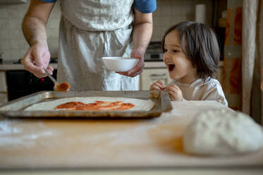 Fröhlicher Junge mit Vater bei der Zubereitung einer Pizza zu Hause - ANAF00290