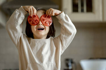 Glücklicher Junge hält Tomatenscheiben über die Augen in der Küche zu Hause - ANAF00294