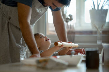 Glücklicher Sohn und Vater rollen Pizzateig in der Küche - ANAF00297