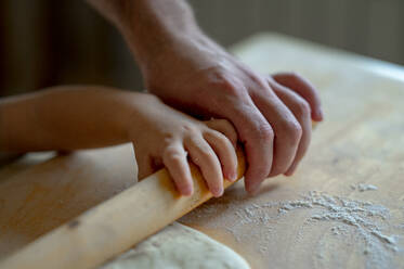 Hand of baby boy and father rolling pizza dough in kitchen at home - ANAF00298