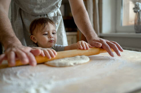 Mann mit kleinem Jungen rollt Pizzateig in der Küche zu Hause - ANAF00299