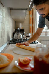 Mann rollt Pizzateig in der Küche zu Hause aus - ANAF00302