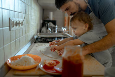 Vater und Sohn rollen gemeinsam Pizzateig in der heimischen Küche aus - ANAF00305