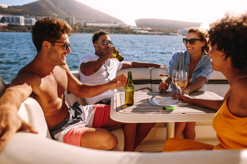 Eine Gruppe von Männern und Frauen feiert eine Bootsparty. Glückliche junge Freunde sitzen hinten auf einer Yacht und trinken. - JLPSF18404