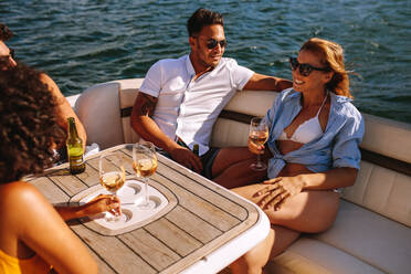 Eine Gruppe junger Männer und Frauen, die sich auf einer Yachtparty vergnügen. Junge Freunde feiern auf einem Boot. Sie sitzen im hinteren Teil des Bootes und trinken Wein. - JLPSF18406