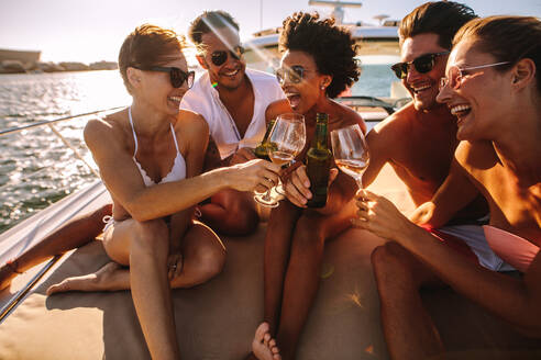 Eine gemischtrassige Gruppe von Menschen stößt mit Getränken auf dem Yachtdeck an und lacht. Fröhliche Männer und Frauen feiern auf einem Boot. - JLPSF18411
