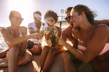 Eine Gruppe fröhlicher Männer und Frauen stößt mit Getränken auf dem Yachtdeck an. Multiethnische Menschen feiern auf einem Boot mit Getränken. - JLPSF18412