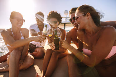 Group of cheerful men and women toasting drinks on the yacht deck. Multi-ethnic people partying on a boat with drinks. - JLPSF18412