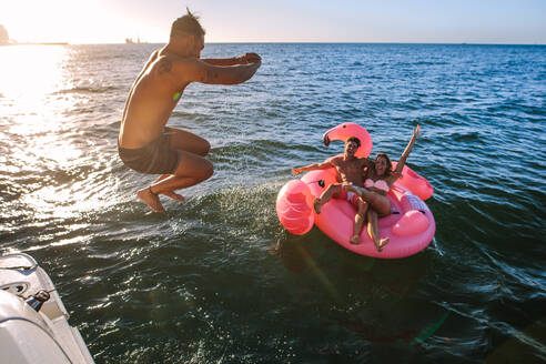 Mann taucht im Meer mit Freunden, die auf einem aufblasbaren Spielzeug sitzen. Gruppe von Freunden, die einen Sommertag genießen. - JLPSF18414