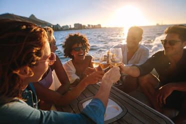 Cheerful young people on yacht drinking together. Group of friends toasting drinks and having party on boat. - JLPSF18415