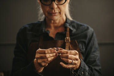 Nahaufnahme der Hände einer Juwelierin, die einen Silberring in der Werkstatt untersucht. Eine Goldschmiedin untersucht Schmuck. - JLPSF18421