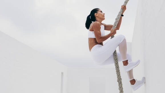 Fitness Frau macht Krafttraining klettern eine Wand mit einem Seil. Frau in Fitness-Kleidung tun Training mit einem Kampf Seil. - JLPSF18467