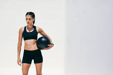 Fitness-Frau steht mit einem Medizinball in der Hand und schaut weg. Frau in Fitnesskleidung macht Workout mit einem Medizinball. - JLPSF18491