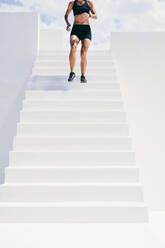 Ausschnitt einer Frau in Fitnesskleidung, die die Treppe hinunterläuft. Fitness-Frau beim Training, die die Treppe eines Gebäudes hinunterläuft. - JLPSF18502