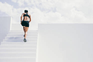 Rückansicht einer Sportlerin, die die Treppe eines Gebäudes hinaufläuft. Frau in Fitnesskleidung beim Workout auf der Treppe. - JLPSF18503