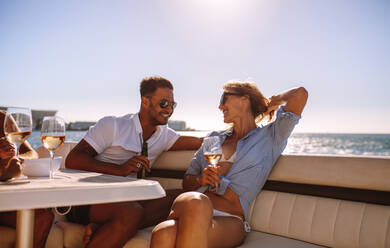 Smiling couple sitting on a boat with drinks. Relaxed young people during a boat party. - JLPSF18510