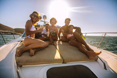 Eine Gruppe glücklicher junger Leute sitzt auf dem Deck einer Yacht und segelt im Meer. Männer und Frauen entspannen sich auf einem kleinen Bootsdeck mit Getränken. - JLPSF18520