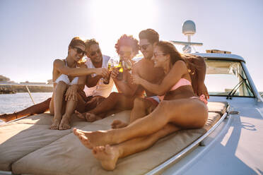 Eine Gruppe lächelnder junger Leute sitzt auf dem Deck und trinkt Wein beim Segeln im Meer. Männer und Frauen feiern eine Bootsparty an einem Sommertag. - JLPSF18524