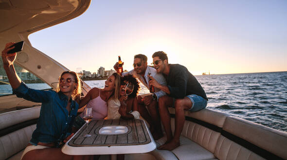 Gruppe von Männern und Frauen, die sich auf einer Yacht mit Getränken entspannen und ein Selfie machen. Multi-ethnische Freunde machen ein Selfie während einer Bootparty. - JLPSF18532