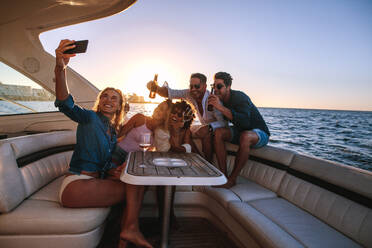 Eine Frau macht ein Selfie mit Freunden auf einer Bootsparty, eine Gruppe junger Leute auf einer Yacht mit Getränken und einem Selfie. - JLPSF18533