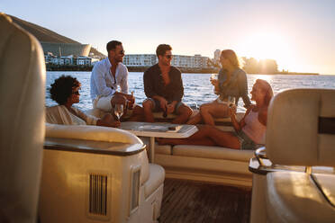 Portrait of young people sitting on a private yacht and drinking. Friends having boat party at sunset. - JLPSF18536