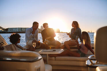 Junge reiche Freunde trinken Wein und Bier auf einer Bootsparty bei Sonnenuntergang. Eine Gruppe junger Leute feiert auf einer Yacht. - JLPSF18537