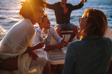 Fröhliche junge Frau trinkt Wein, während sie mit Freunden auf einem Boot sitzt. Frau genießt eine Bootsparty mit Freunden. - JLPSF18540