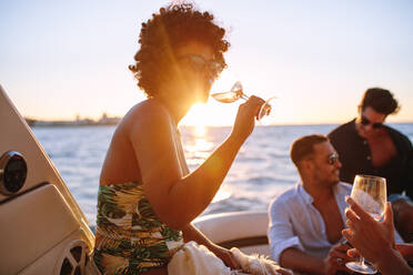 African woman drinking during sunset boat party with friends. Group of men and women having a boat party during sunset. - JLPSF18542