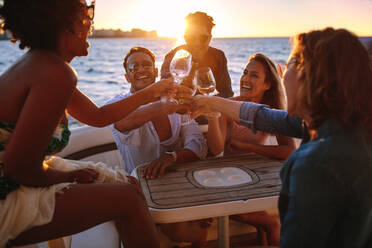 Multi-ethnic group of people on yacht drinking together. Group of friends toasting drinks at sunset boat party. - JLPSF18544