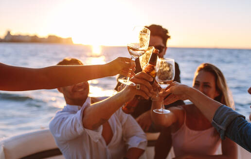 Bootsparty bei Sonnenuntergang mit jungen Leuten, die mit Getränken anstoßen. Gruppe von Männern und Frauen bei einer Bootsparty. - JLPSF18546