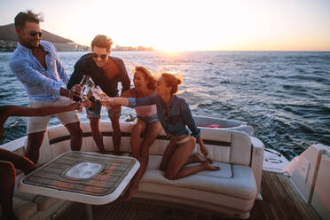 Group of young people sitting at the back of a yacht and toasting drinks. Young people having a boat party at sunset. - JLPSF18550