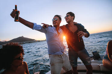 Männer, die sich auf einer Bootsparty bei Sonnenuntergang amüsieren. Freunde feiern auf einer Yacht mit Getränken. - JLPSF18552