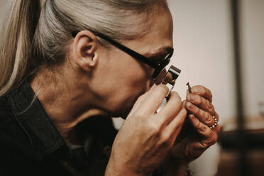 Close up of woman jeweler examining diamond through loupe at workshop. close-up Senior female jeweler looking at diamond through magnifying loupe. - JLPSF18579